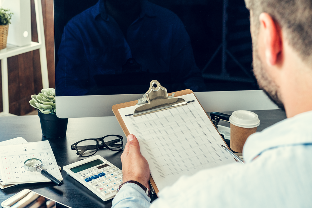 Man reviewing financial data on clipboard at desk.